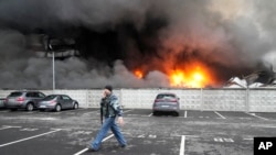 FILE - A Ukrainian serviceman walks past as fire and smoke rises over a damaged logistic center after shelling in Kyiv, Ukraine, March 3, 2022.