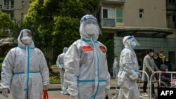 Pekerja dan sukarelawan melihat ke dalam kompleks tempat warga yang melakukan tes COVID-19 di Shanghai. (Foto: AFP)