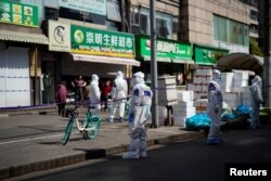 Polisi dan anggota keamanan mengenakan APD berdiri di luar toko makanan yang ditutup di tengah pandemi COVID-19di Shanghai, China 29 Maret 2022. (REUTERS/Aly Song)