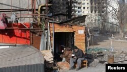 Local residents have a meal outside a building damaged during Russia's invasion of Ukraine, in the besieged southern port city of Mariupol, March 31, 2022. According to U.N. agencies, food supplies are dwindling in Ukraine.