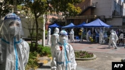 身穿防护服的工作人员在上海静安区的一个测试点看着居民做新冠病毒测试。（2022年4月4日）