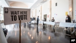 FILE - Polling location workers await a rush of lunchtime voters in the U.S. Senate runoff election, Dec. 6, 2022, in Atlanta. 