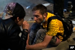 FILE - Homeless addicts Brandice Josey, left, uses a straw to blow a puff of fentanyl smoke into the mouth of Ryan Smith, who is high on the drug, in Los Angeles, Aug. 18, 2022.