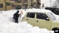 A resident shovels snow off around a car at a parking lot in Kitami city Hokkaido prefecture, northern Japan, on Dec. 24 2022.