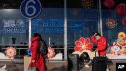 Pelancong yang mengenakan masker dengan membawa barang bawaan mereka berjalan melalui gerbang masuk terminal keberangkatan penerbangan internasional di bandara Beijing, 29 Desember 2022. (AP/Andy Wong)