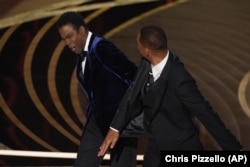 Will Smith, right, hits presenter Chris Rock on stage while presenting the award for best documentary feature at the Oscars on Sunday, March 27, 2022, at the Dolby Theatre in Los Angeles. (AP Photo/Chris Pizzello)