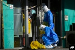Workers in protective gear prepare to collect COVID samples from a woman at her locked down store in Beijing, Dec. 1, 2022.