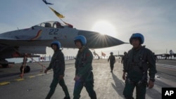 中国海军第二艘、也是第一艘完全由本国建造的002型山东号航母。照片显示山东号停泊在三亚军港，飞行员走在甲板上。-新华社照片