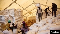 FILE: Men carry bags of food while women wait for their rations at a food distribution site in Pibor, South Sudan, June 25, 2012.