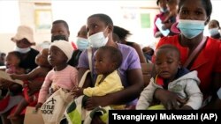 Women holding babies take their places on wooden benches at a clinic in Harare, Zimbabwe, Thursday, Sept. 15, 2022. 