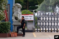 A security guard smokes near a main entrance gate of the Ganzhou Huajian International Shoe City Co.'s factory, which has made shoes for the Ivanka Trump brand, in Ganzhou in southern China's Jiangxi province, June 18, 2017. The sign instructs visitors to "please exit the vehicle and register. People without relevant reasons cannot enter this important factory area."