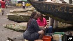 FILE - Fishmongers sit next to boats as they prepare freshly caught fish to be smoked on Limbe beach, Cameroon, Apr. 12, 2022.