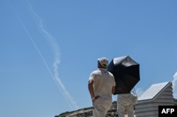 FILE - Smoke trails from projectiles launched by the Chinese military are seen in the sky as tourists look on from Pingtan Island, one of mainland China's closest point from Taiwan, in Fujian province on Aug. 4, 2022.