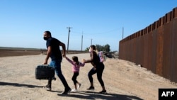 Satu keluarga migran dari Kuba tampak berlari di wilayah perbatasan antara AS dan Meksiko untuk menyerahkan diri mereka kepada petugas berwenang di Yuma, Arizona, pada 13 Mei 2021. (Foto: AFP/Ringo Chiu)