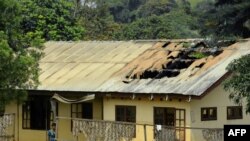 FILE - A woman stands outside the damaged roof of a school's dormitory, after it was set to fire overnight in Bafut, in the northwest English-speaking region of Cameroon, Nov. 15, 2017.