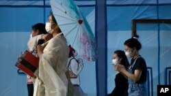 FILE - People wearing face masks walk through a plaza at an outdoor shopping mall in Beijing, July 23, 2022. 