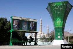 FILE - People sit under posters of Houthi leaders in Sanaa, Yemen, April 7, 2022.