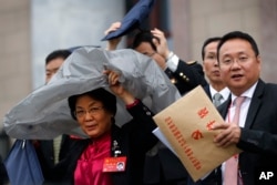 A female delegate uses a plastic cover to shield from the rain as she leaves the Great Hall of the People with others after attending the opening ceremony of the 19th Party Congress in Beijing, Oct. 18, 2017.
