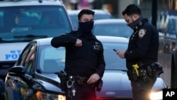 Police officers stand at the intersection of Main Street and Roosevelt Avenue as pedestrians pass them in the Flushing neighborhood of the Queens borough of New York, March 30, 2021.