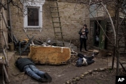 A woman holds her cat as she walks next to the bodies of her husband, brother, and another man, who were killed outside her home in Bucha, on the outskirts of Kyiv, Ukraine, April 4, 2022.