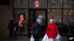FILE - Two women walk past a currency exchange office screen displaying the exchange rates of U.S. dollar and euro to Russian rubles in Moscow, Russia, April 1, 2022.