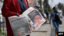 Los peatones pasan frente a un vendedor que vende diarios locales que llevan los titulares que informan la noticia de la muerte de la reina Isabel II, en Nairobi el 9 de septiembre de 2022.