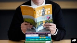 FILE - Amanda Darrow, director of youth, family and education programs at the Utah Pride Center, poses with books that have been the subject of complaints from parents, in Salt Lake City, Utah, Dec. 16, 2021.