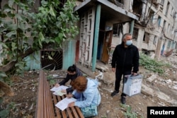Local residents fill out documents before casting their votes into a mobile ballot box carried by an election official during a Moscow-orchestrated referendum on Russian-controlled regions of Ukraine joining Russia, in Mariupol, Ukraine, Sept. 24, 2022.