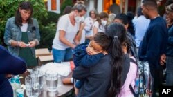 A woman, who is part of a group of immigrants that had just arrived holds a child as they are fed outside St. Andrews Episcopal Church, Sept. 14, 2022, in Edgartown, Mass., on Martha's Vineyard. (Ray Ewing/Vineyard Gazette via AP)