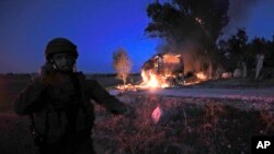 An Israeli soldier stands near a burning bus after it was hit by a mortar shell fired from Gaza near the Israel Gaza border, Nov. 12, 2018.