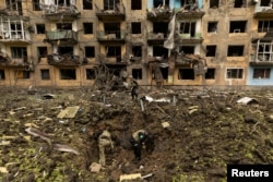 Ukrainian military personnel inspect the site of a missile strike in front of a damaged residential building in Dobropillia, in the Donetsk region, Ukraine, April 30, 2022.