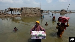 Women carry belongings salvaged from their flooded home after monsoon rains, in the Qambar Shahdadkot district of Sindh Province, of Pakistan, Sept. 6, 2022. 