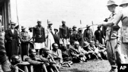 Guarded by members of the Lancashire Fusiliers, police and loyal Kikuyu spearmen, suspected members of the Mau Mau are questioned about the murder of two Europeans near Gilgil, Kenya, on Jan. 8, 1953. 