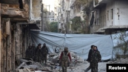 FILE - Syrian government soldiers walk amid rubble of damaged buildings after they took control of al-Sakhour neighborhood in Aleppo, in this handout picture provided by SANA, Nov. 28, 2016.
