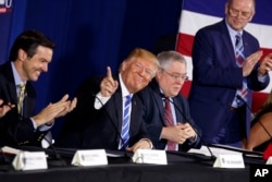 FILE - President Donald Trump, center, smiles as people applaud him during a round-table discussion on tax policy in White Sulphur Springs, W.Va., April 5, 2018.