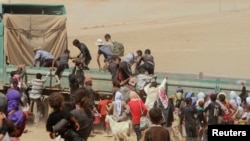 Displaced people from the minority Yazidi sect jump onto a truck as they make their way toward the Syrian border town of Elierbeh of Al-Hasakah Governorate, Aug. 10, 2014.