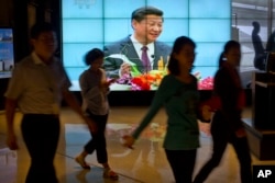 People walk past a large videoscreen showing Chinese President Xi Jinping during his trip to the United States from Chinese state broadcaster CCTV in an office building in Beijing, Sept. 25, 2015.
