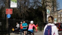 Las personas observan el distanciamiento social cuando pasan por las puertas cerradas del Parque Brockwell en Londres, cerrado durante la noche por el consejo local para ayudar a detener la propagación del coronavirus.