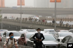 People wearing face masks walk past cars clogged with heavy traffic on a road as Beijing is hit by polluted air and sandstorm, May 4, 2017. Authorities in Beijing issued a blue alert on air pollution as sandstorm swept through the Chinese capital city on Thursday.
