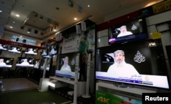 FILE - Nasr al-Ansi, a leader of the Yemeni branch of al-Qaida in the Arabian Peninsula, is shown on televisions at a shop, delivering a message in which AQAP claims responsibility for the attack on the French magazine Charlie Hebdo, in Sana'a, Yemen, Jan. 14, 2015.