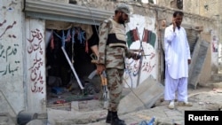 An army soldier stands with a police officer in front of a damaged Pakistan People's Party (PPP) election campaign office after a bomb blast, in Quetta, May 10, 2013.
