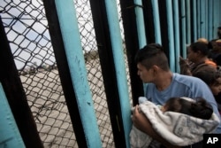 FILE - A member of the Central American migrant caravan, holding a child, looks through the border wall toward a group of people gathered on the U.S. side, as he stands on the beach where the border wall ends in the ocean, in Tijuana, Mexico, April 29, 2018.
