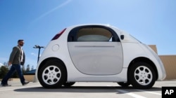 A reporter walks toward a Google self-driving prototype car during a demonstration at the Google campus in Mountain View, California, May 13, 2015.