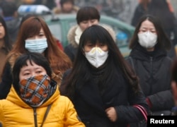 FILE - Commuters wearing masks make their way amid thick haze in the morning in Beijing, Feb. 26, 2014.