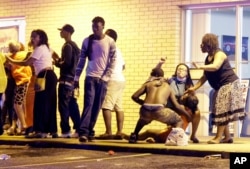 Warga membantu seorang perempuan yang histeris setelah sebuah tembakan terdengar dekat sebuah demonstrasi di Ferguson, Missouri, MInggu (9/8).