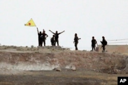 Fighters with the Kurdish People's Protection Units, or YPG, wave their yellow triangular flag on the outskirts of Tal Abyad, Syria, June 15, 2015.