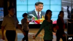 People walk past a large videoscreen showing Chinese President Xi Jinping during his trip to the United States from Chinese state broadcaster CCTV in an office building in Beijing, Sept. 25, 2015.