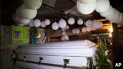 Balloons hang over the coffin that contain the remains of 7-year-old Jakelin Caal Maquin during a memorial service in her grandparent's home in San Antonio Secortez, Guatemala, Monday, Dec. 24, 2018. 