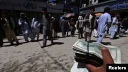 FILE - A money changer holds a stack of U.S. dollars at Kabul's largest money market April 23, 2014. The U.S. has reportedly spent $113 billion rebuilding Afghanistan, more than it spent rebuilding Europe after World War II, adjusted for inflation.
