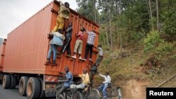FILE - Young people on bicycles hang to the back of a truck July 19, 2015, outside the capital Bujumbura, Burundi.
